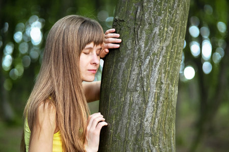 Young woman leaning to tree trunk in summer forest.の写真素材