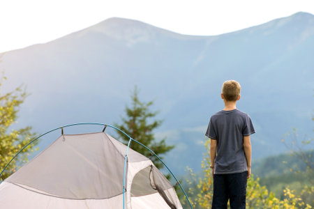 Hiker child boy resting standing near a camping tent at mountains campsite enjoying view of summer nature.の写真素材
