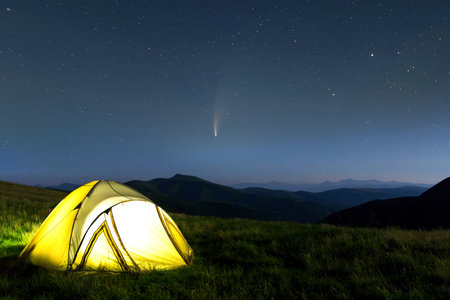 Tourist hikers tent in mountains at night with stars and Neowise comet with light tail in dark night sky.の写真素材