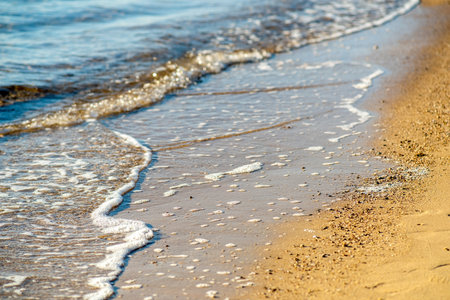 Close up of small sea waves with clear blue water over yellow sand beach at summer sunny shore.の写真素材