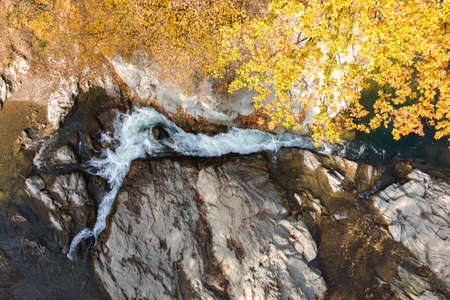 Top down aerial view of small mountain stream with fast moving clear water between rocky stones in...