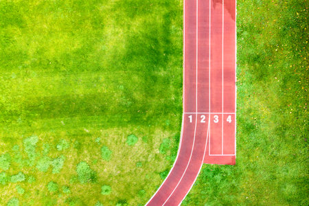 Aerial view of sports stadium with red running tracks with numbers on it and green grass football...