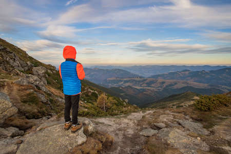 Young child boy hiker standing in mountains enjoying view of amazing mountain landscape.の写真素材