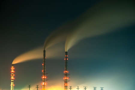 Brightly illuminated coal power plant high pipes with black smoke moving upwards polluting atmosphere at night with reflections of it in lake water.の写真素材