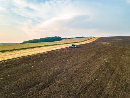 Aerial view of a tractor plowing black agriculture farm field after harvesting in late autumn.の写真素材