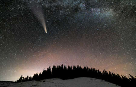 Surreal view of night in mountains with starry dark blue cloudy sky and C / 2020 F3 (NEOWISE) comet with light tail.の写真素材