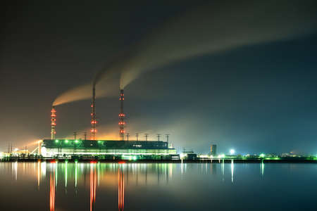 Brightly illuminated coal power plant high pipes with black smoke moving upwards polluting...