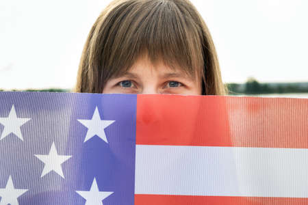 Portrait of happy smiling girl hiding her face behind USA national flag.