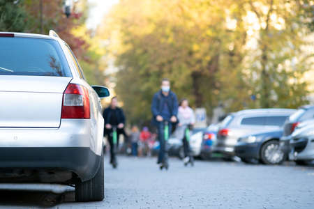 Cars parked in a row on a city street side on bright autumn day with blurred people walking on...