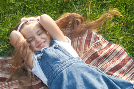 Pretty little child girl with closed eyes laying down on blanket on green grass in summer taking a nap.の写真素材