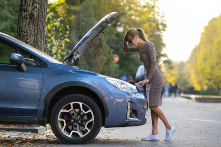 Female driver opening car hood inspecting broken engine on a city street.の写真素材