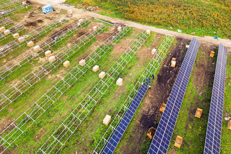 Aerial view of solar power plant under construction on green field. Assembling of electric panels...