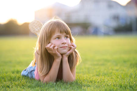 Young pretty child girl laying down on green grass lawn on warm summer day.の写真素材