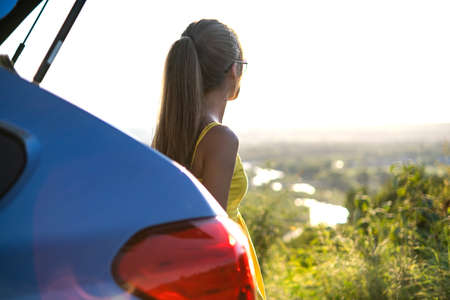 Happy woman driver in summer dress enjoying warm evening near her car. Travel and vacation concept.の写真素材