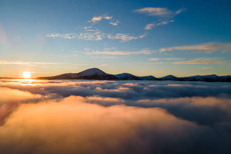 Aerial view of vibrant sunrise over white dense fog with distant dark Carpathian mountains on horizon.の写真素材