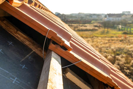 Closeup of metal montage anchor for installation of yellow ceramic roofing tiles mounted on wooden...