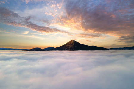 Aerial view of vibrant yellow sunrise over white dense clouds and distant mountains on horizon.の写真素材