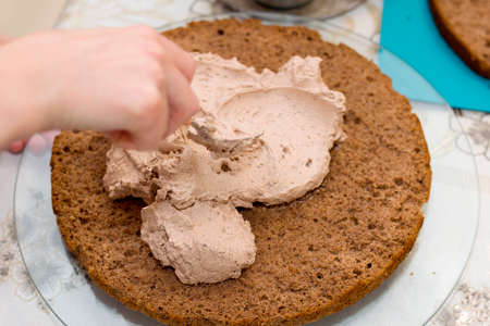 Working process of baking cake at home. Close up of female hand topping cream on chocolate biscuit. Culinary and delicious dessert concept.の写真素材