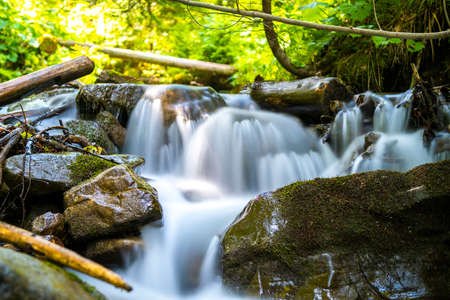 Mountain river with small waterfall with clear turquoise water falling down between wet boulders...