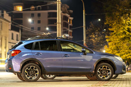 Blue car parked on brightly illuminated city street at night.