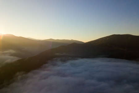 Aerial view of vibrant sunrise over white dense fog with distant dark silhouettes of mountain hills...