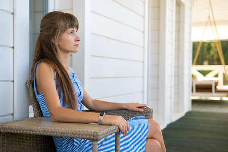 Side view of young beautiful woman resting on fresh air sitting on porch at home. Concept of enjoying nature with good weather.の写真素材