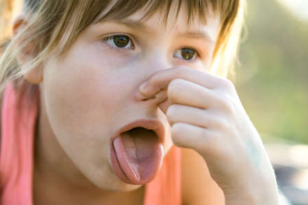 Close up of portrait beautiful child girl pinching nose and showing tongue.の写真素材