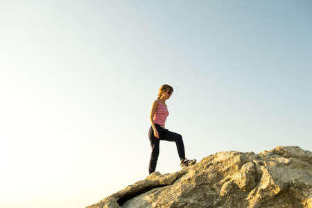 Woman hiker climbing steep big rock on a sunny day. Young female climber overcomes difficult climbing route. Active recreation in nature concept.の写真素材