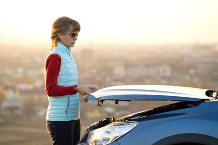 Young woman opening bonnet of broken down car having trouble with her vehicle. Female driver near...
