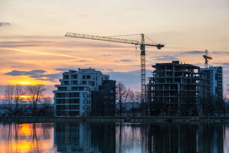 Tower cranes and high residential apartment buildings under construction on lake shore. Real estate...