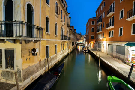 Night scene of illuminated old buildings, floating boats and reflections in canal water in Venice, Italy.の写真素材