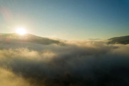 Aerial view of vibrant sunset over white dense foggy clouds with distant dark silhouettes of mountains on horizon.の写真素材