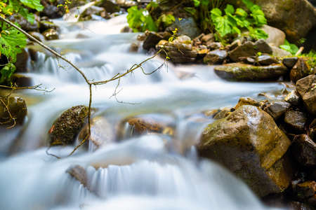 Mountain river with small waterfall with clear turquoise water falling down between wet boulders with thick white foam.の写真素材