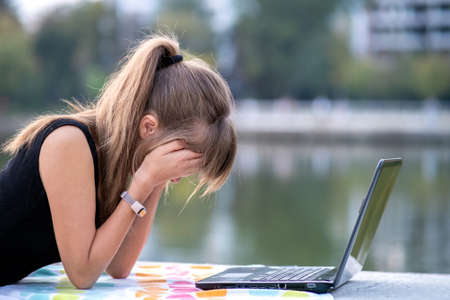 Tired female office employee working behind laptop computer lying down in summer park outdoors....