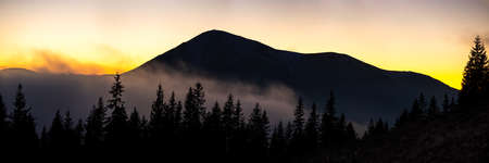Beautiful mountain panorama of landscape with hazy peaks and foggy wooded valley at sunset.の写真素材