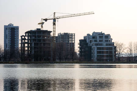 Tower cranes and high residential apartment buildings under construction on lake shore. Real estate development.の写真素材