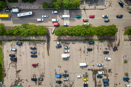 Top down aerial view of busy street with moving cars traffic and big parking lot with many parked...