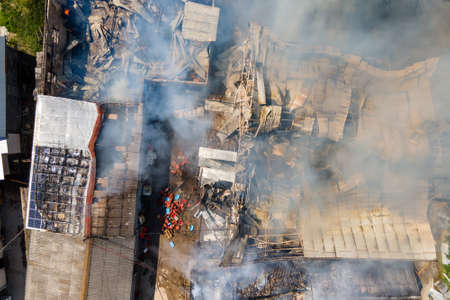Aerial view of ruined building on fire with collapsed roof and rising dark smoke.