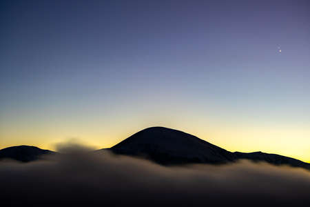 Beautiful mountain landscape with hazy peaks and foggy valley at sunset.