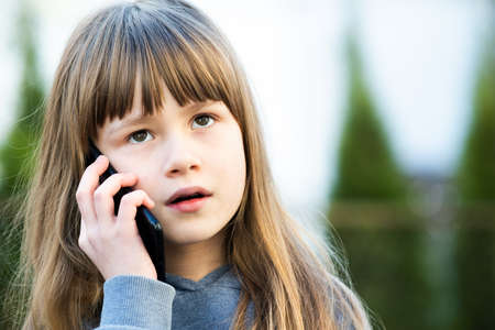 Portrait of pretty child girl with long hair talking on cell phone. Little female kid communicating...