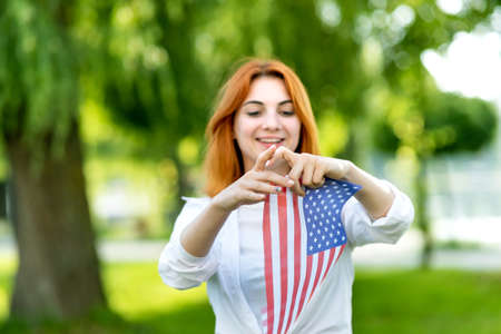 Happy young woman posing with USA national flag standing outdoors in summer park. Positive girl with...