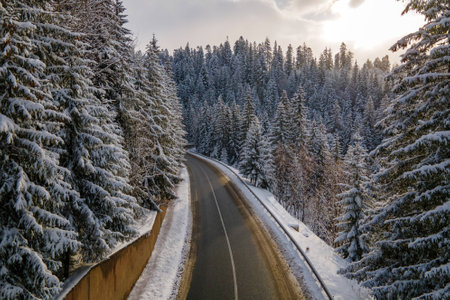Aerial view of winter landscape with snow covered mountain hills and winding forest road in morning.