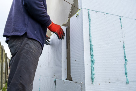 Construction worker installing insulation sheets on house facade wall for thermal protection.の写真素材