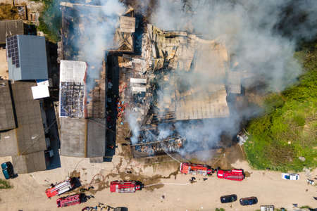 Aerial view of firefighters extinguishing ruined building on fire with collapsed roof and rising...