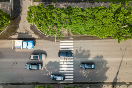 Top down aerial view of busy street with moving cars traffic and zebra road pedestrian crosswalk.