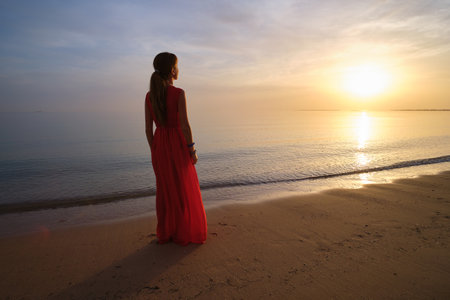 Lonely young woman standing on ocean beach by seaside enjoying warm tropical evening.の写真素材