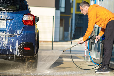 Young driver man washing his car with contactless high pressure water jet in self service car wash.の写真素材