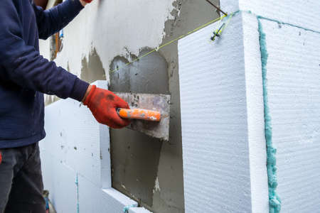 Construction worker installing styrofoam insulation sheets on house facade wall for thermal protection.の写真素材