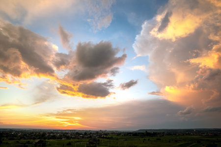 Dramatic sunset rural landscape with puffy clouds lit by orange setting sun and blue sky.の写真素材