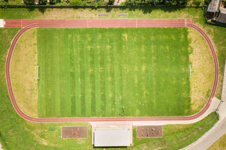 Aerial view of sports stadium with red running tracks and green grass football field.